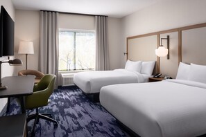 Ein Hotelzimmer mit zwei Betten, einem Schreibtisch, einem Stuhl, einem Fernseher und einem Fenster mit Vorhängen.