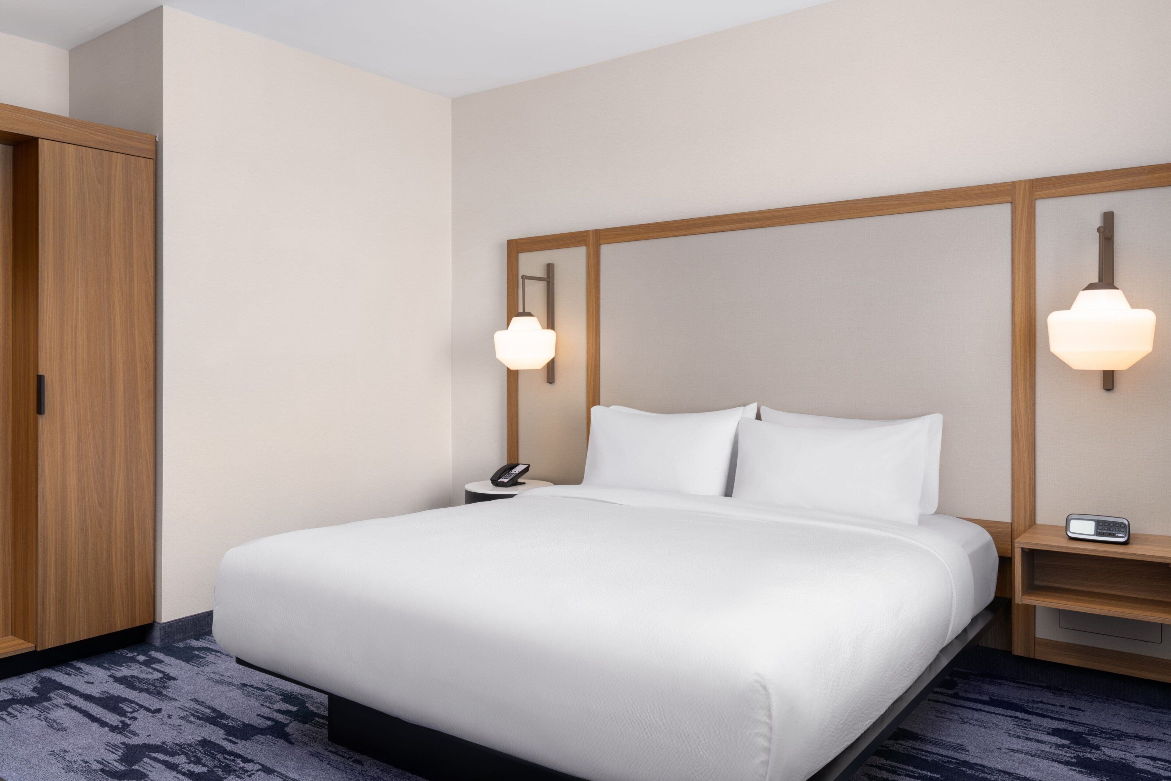 A hotel room with a large bed, wooden headboard, bedside tables with lamps, and a wardrobe.