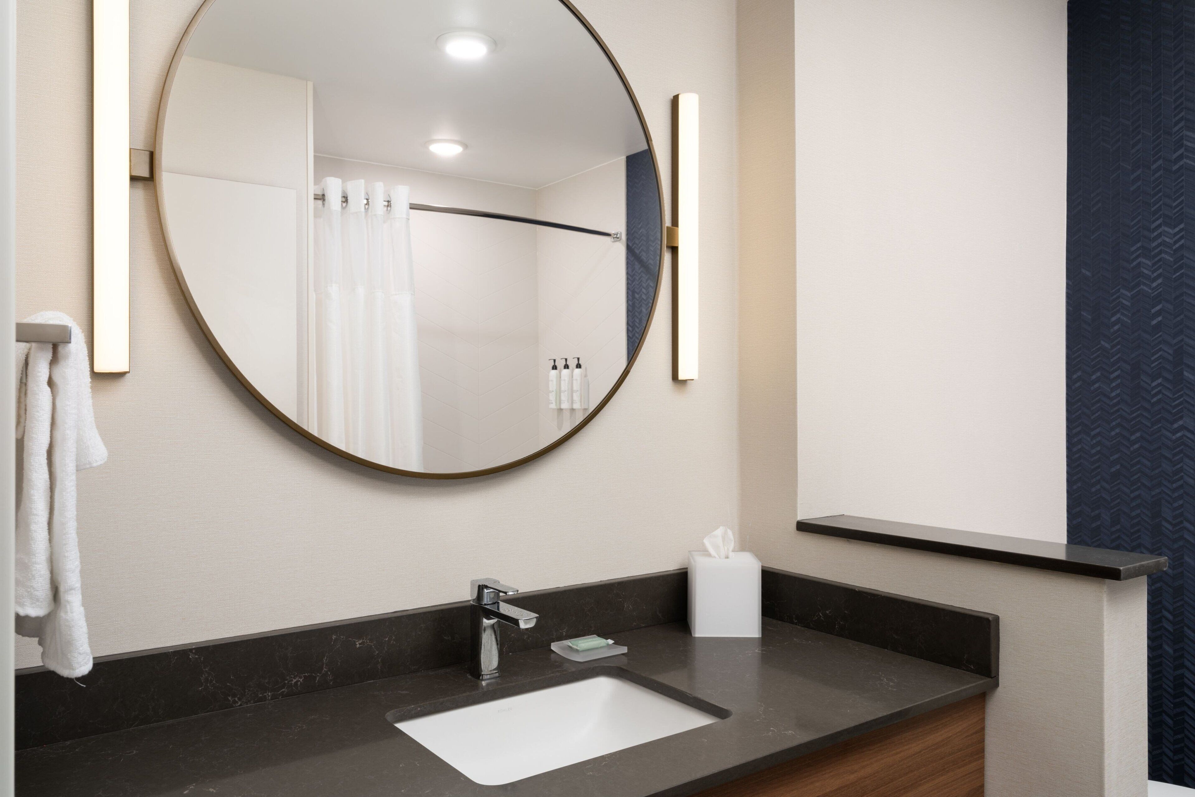Un baño moderno con un espejo redondo, un lavabo blanco, un perchero y un dispensador de pañuelos.