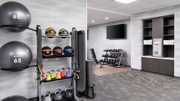 A gym with exercise equipment, including a rack of dumbbells and medicine balls, and a TV mounted on the wall.