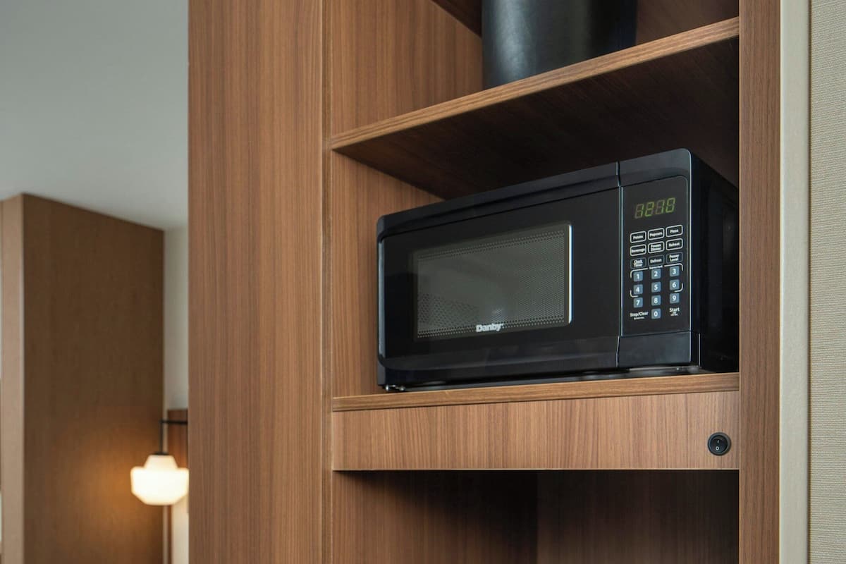 A hotel room with a wooden cabinet containing a microwave, a coffee maker, and a bag of coffee.