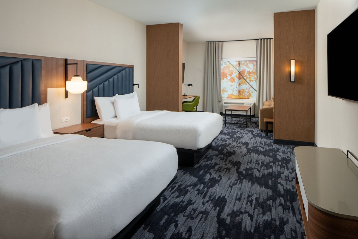 Une chambre d’hôtel avec deux lits, un bureau, une chaise, une télévision et une fenêtre avec des rideaux.