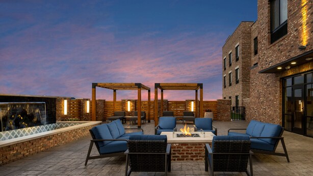 An outdoor patio with brick flooring, blue cushioned seating, a central fire feature, and a brick wall with a window. - Fairfield by Marriott Inn & Suites Southaven Snowden Grove (Southaven)