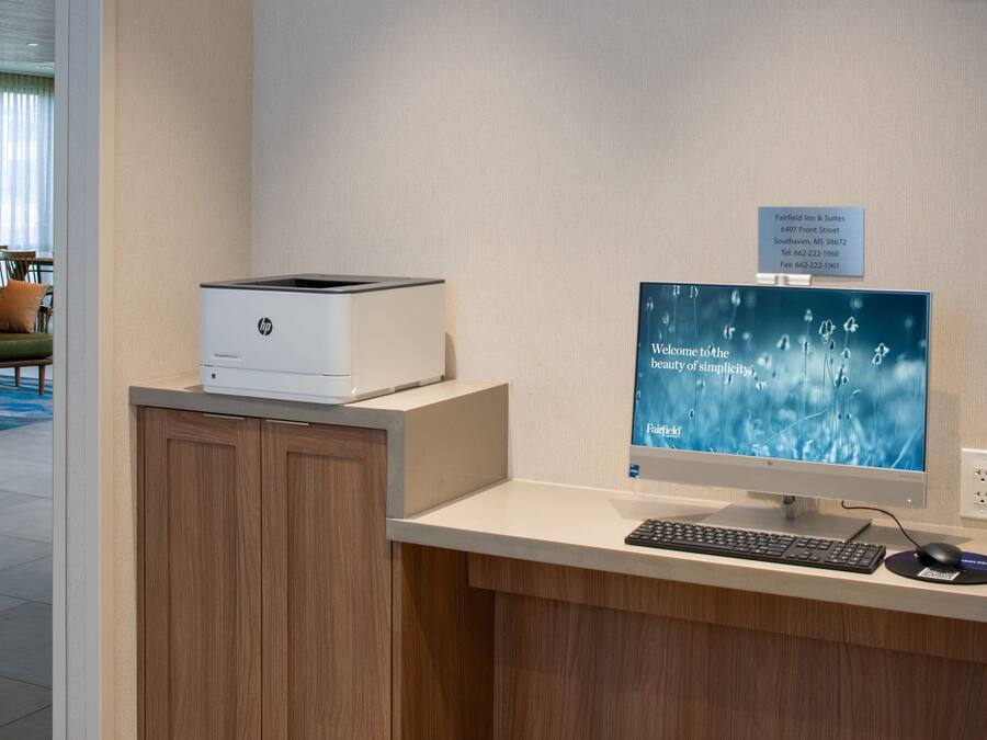 Un comptoir d’accueil d’hôtel équipé d’un ordinateur de bureau, d’une imprimante et d’un panneau indiquant l’adresse de l’hôtel.