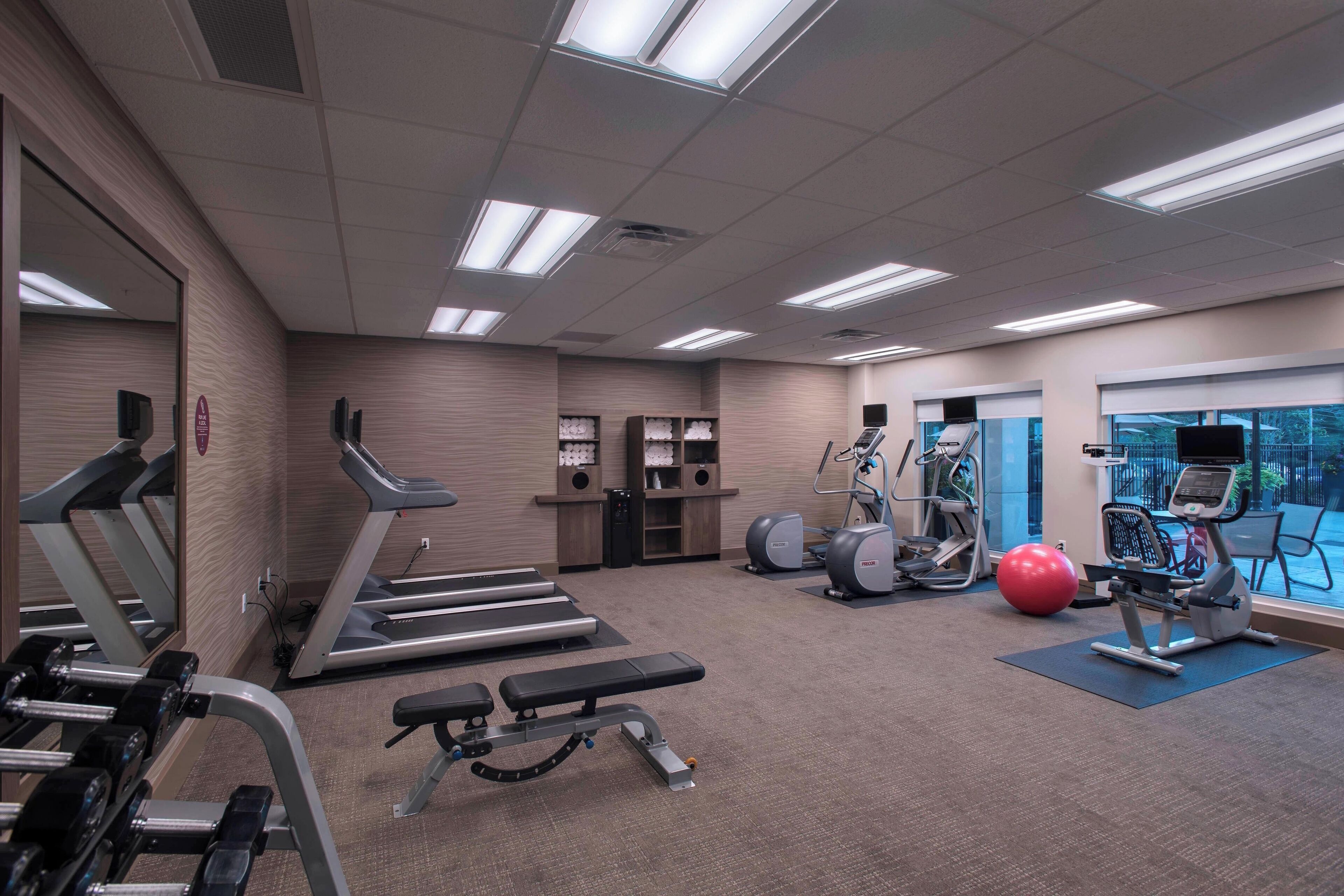 A gym with treadmills, elliptical machines, a bench, and a red exercise ball.