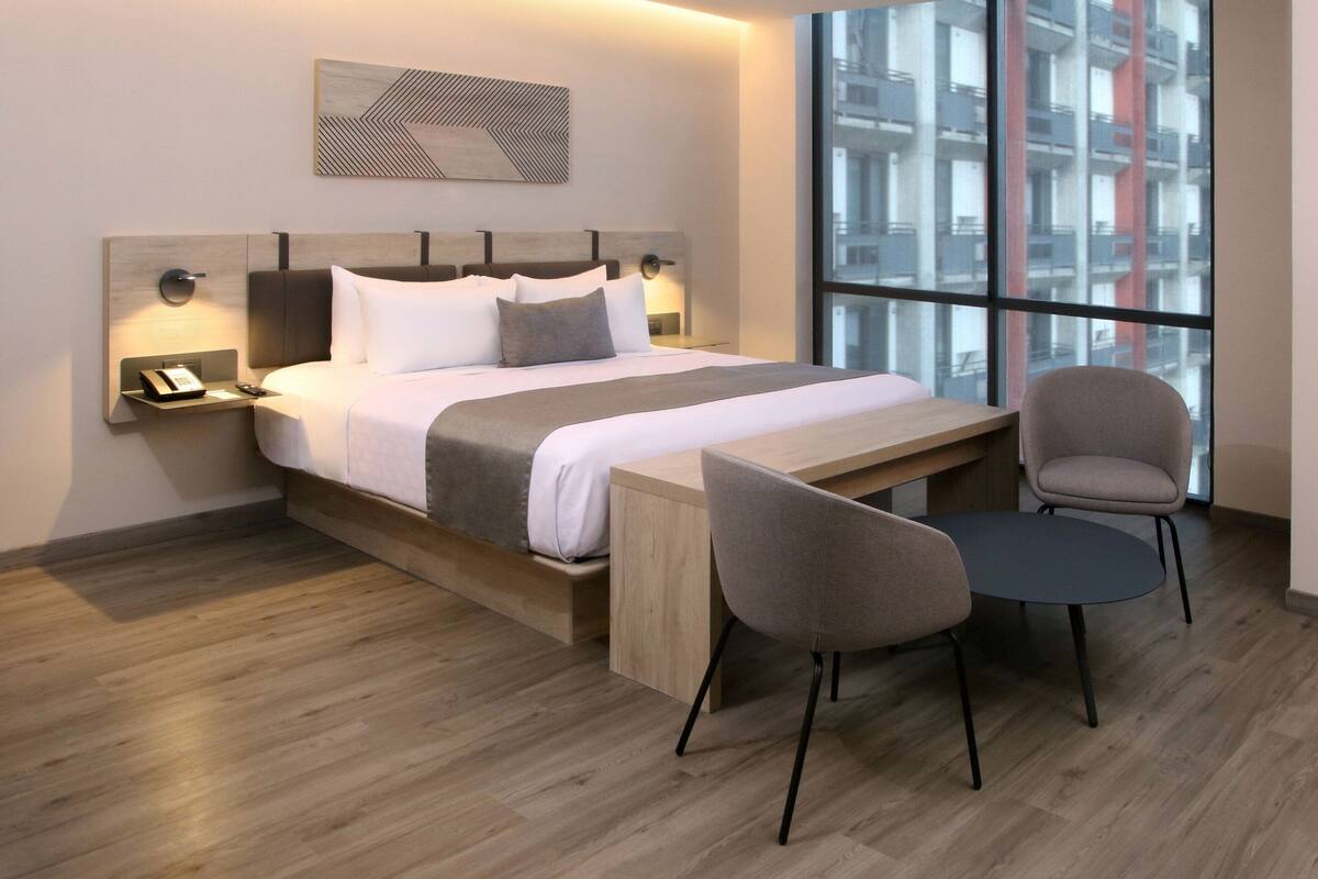 A modern hotel room with a large bed, bedside tables, a desk, and chairs.
