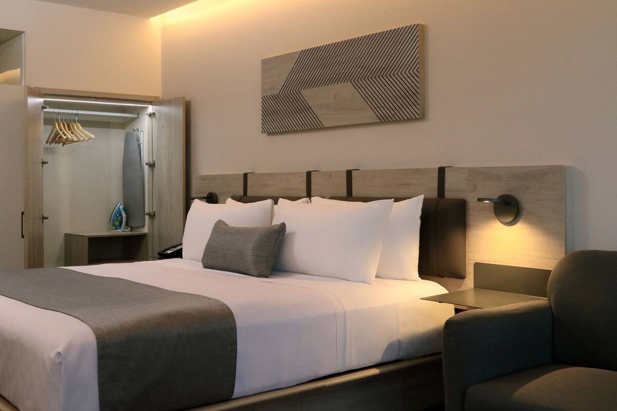 A hotel room with a bed, bedside table, chair, and a wall-mounted artwork.