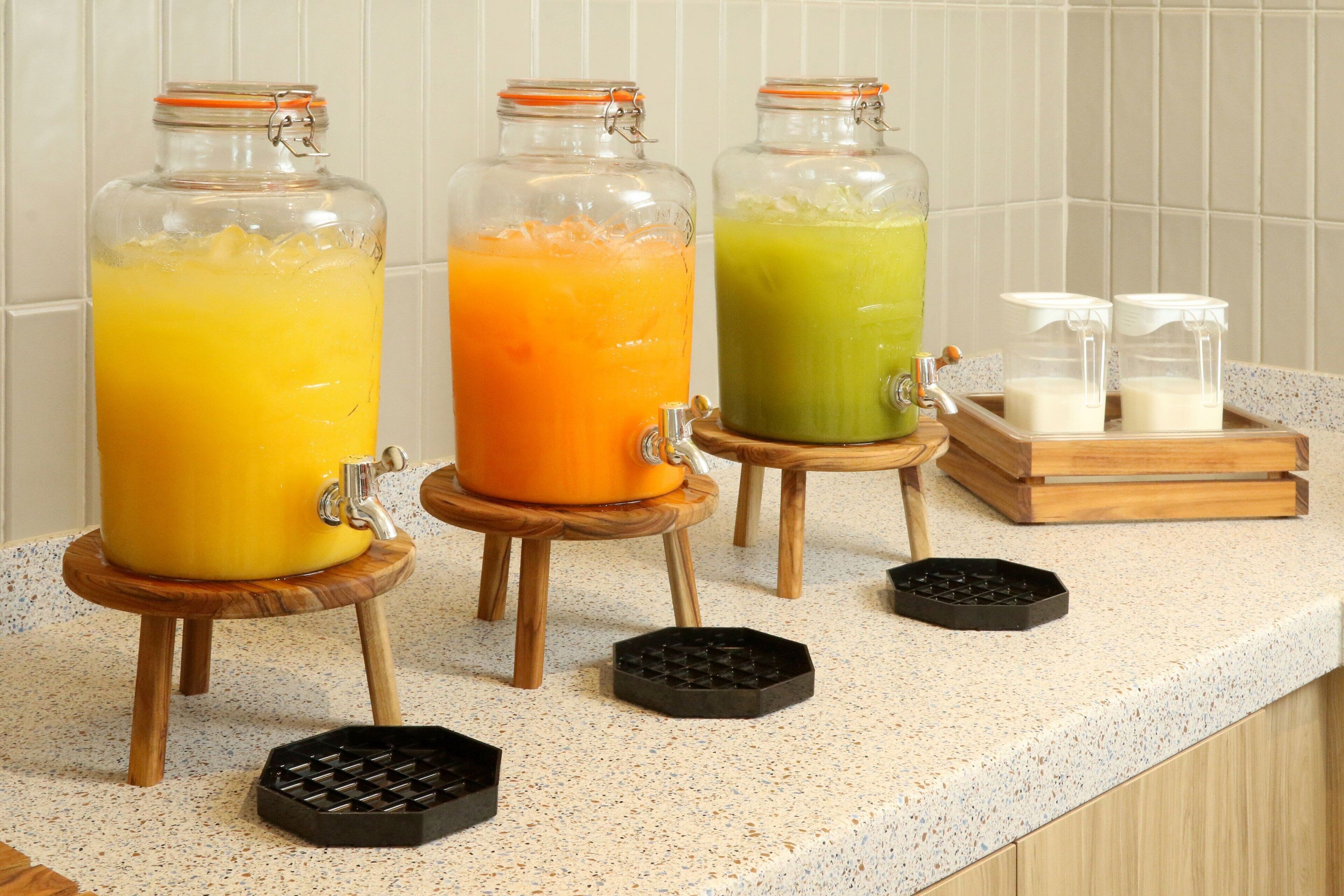 Trois distributeurs en verre contenant différents liquides de couleurs variées, posés sur un plan de travail de cuisine.