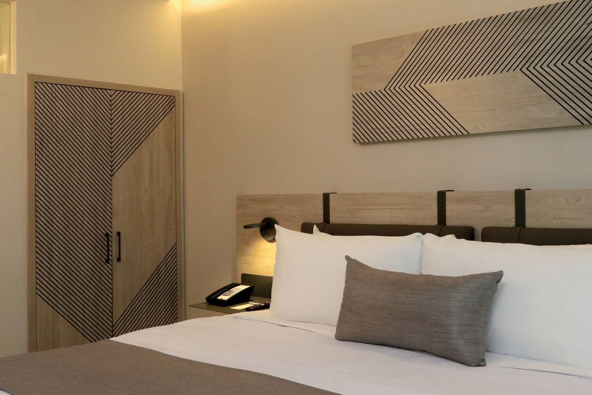 A hotel room with a bed, bedside table, and a geometric-patterned wall art piece above the bed.