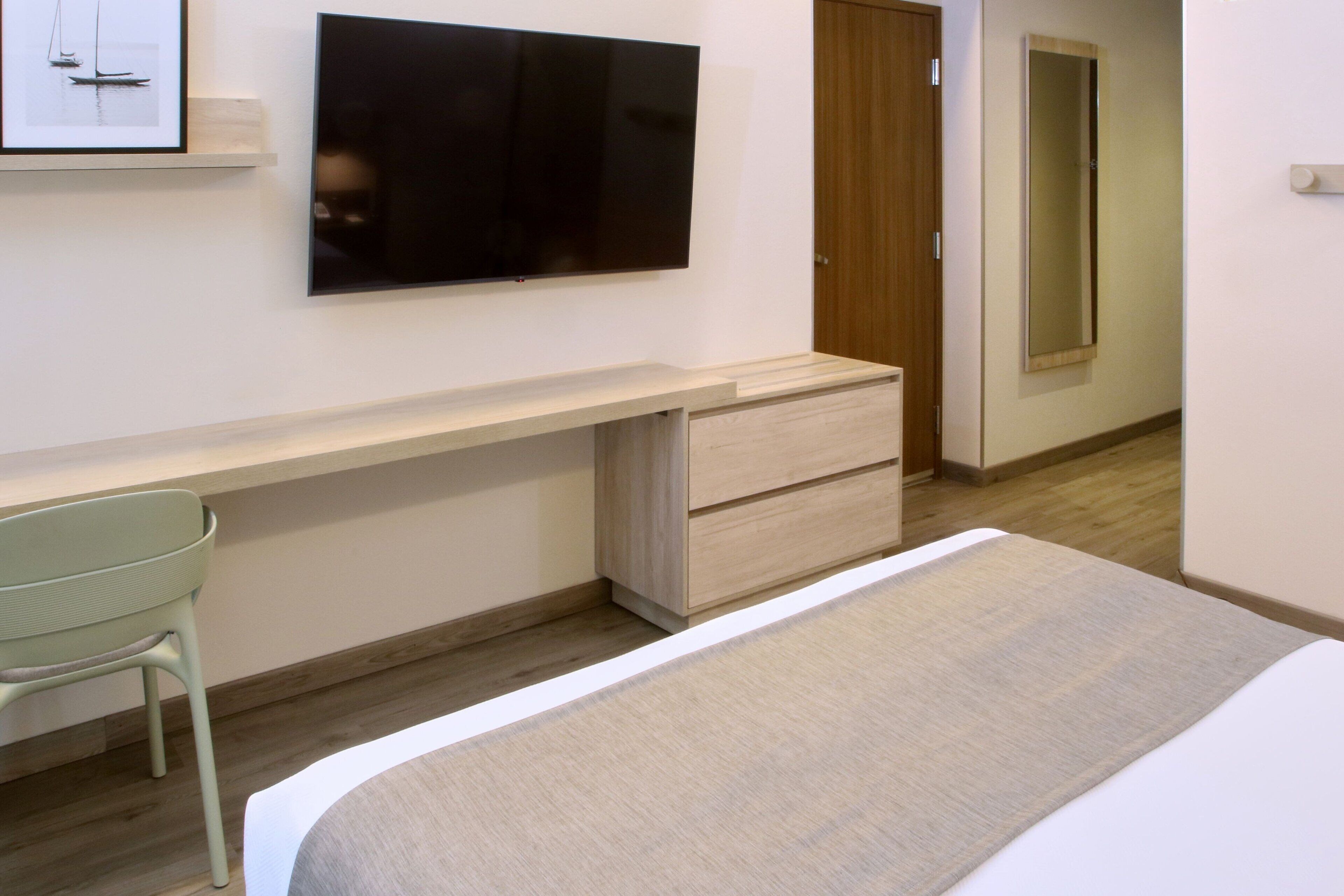 A bedroom with a bed, a desk, a chair, a TV mounted on the wall, and a wardrobe.