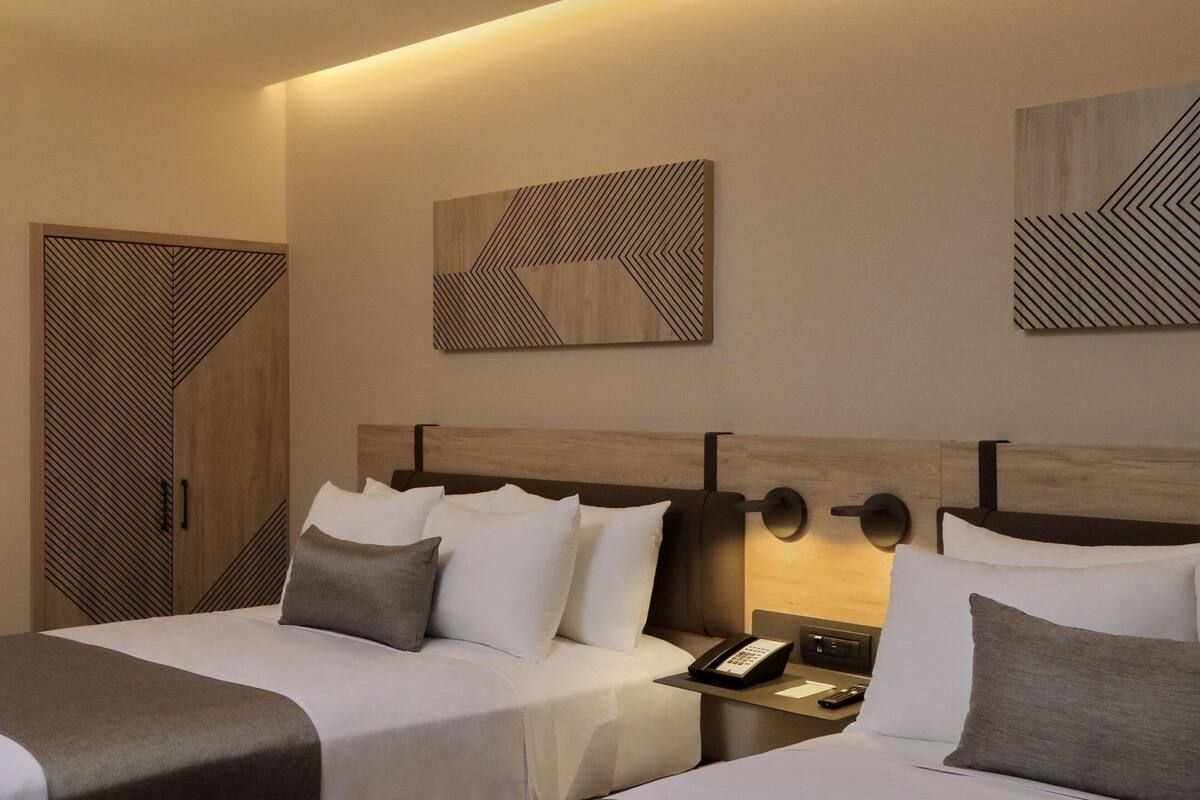A hotel room with two beds, a nightstand with a phone, and wall art.
