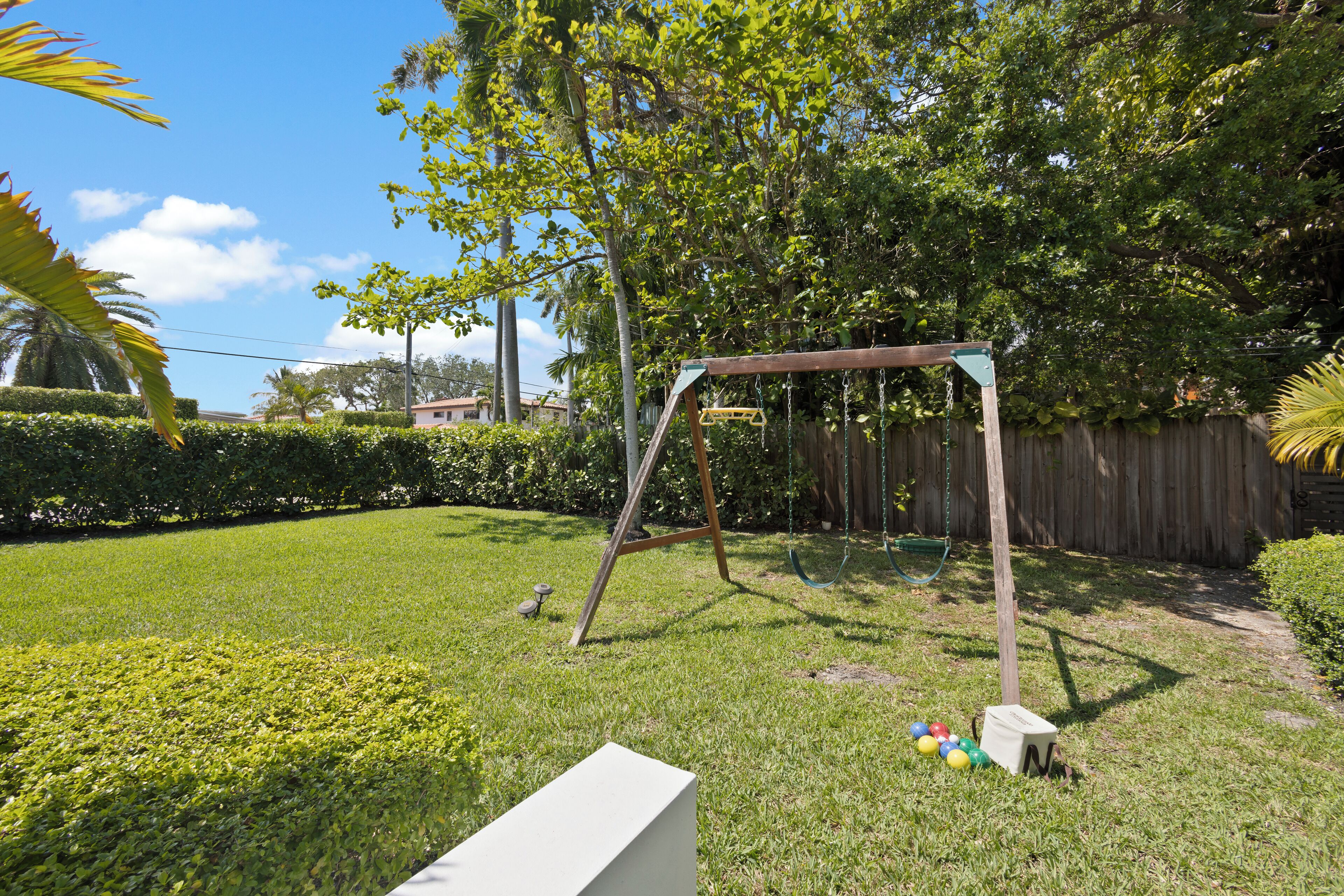 A grassy backyard with a wooden swing set, a fenced area, and a white bench.