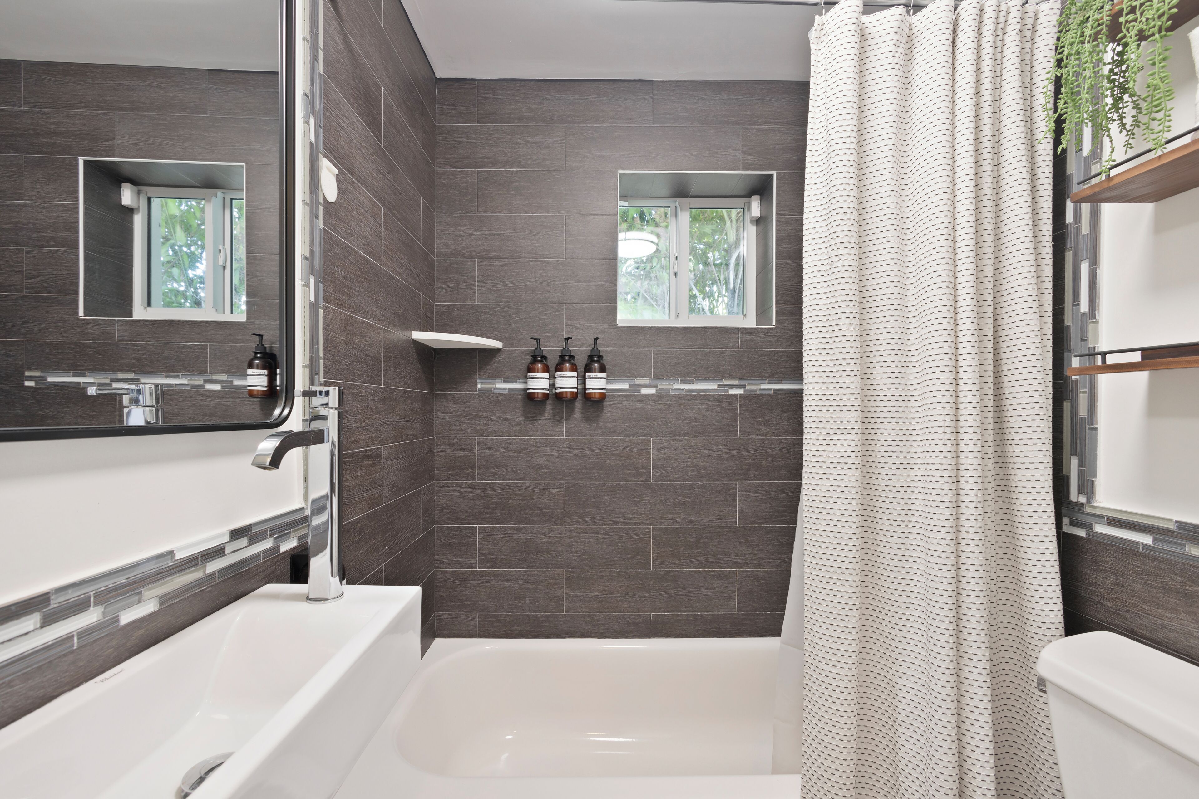 A modern bathroom with a large bathtub, two windows, and a shower curtain.