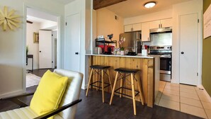 A modern kitchen with wooden accents, a bar area, and a seating space with a yellow cushion.