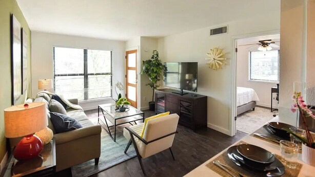 A modern living room with a sofa, coffee table, and TV. There is a dining area with a table set for two.