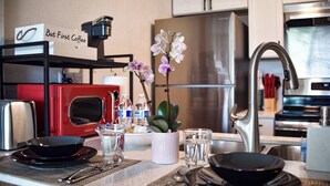 A modern kitchen with a coffee machine, a red oven, a refrigerator, and a sink.