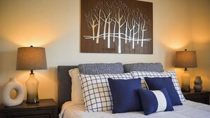 A neatly made bed with a white comforter and blue and white patterned pillows, flanked by two nightstands with lamps and decorative vases.
