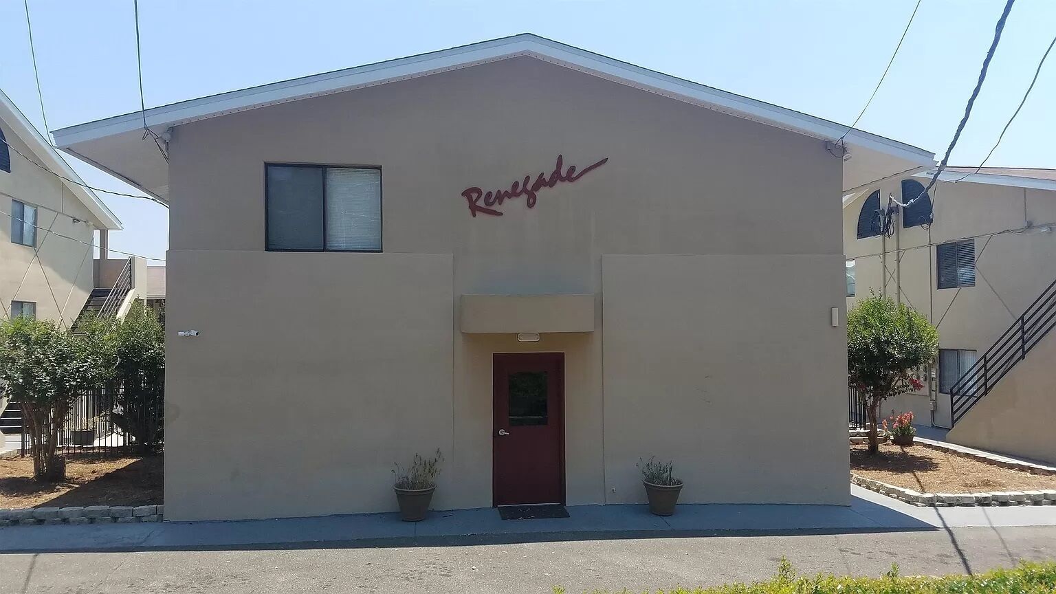 Un bâtiment avec une porte rouge et le nom « Renjade » au-dessus. Deux plantes en pot sont placées devant la porte.