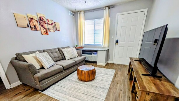 A living room with a grey sofa, a round wooden coffee table, a TV on a wooden stand, and a window with curtains. - Cozy 1/1 Walking distance to Doak Campbell Stadium and campus (Tallahassee)
