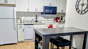 A compact kitchen with white cabinets, a microwave, a stove, and a small dining area with a table and two stools. - Cozy 1/1 Walking distance to Doak Campbell Stadium and campus (Tallahassee)
