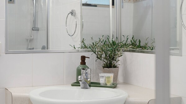 Casa de banho com lavatório branco, dispensador de sabão verde e uma planta em vaso.