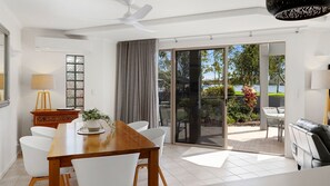Uma zona de refeições moderna com mesa de madeira, cadeiras brancas e vista para um jardim e um espelho de água através de grandes portas de vidro.