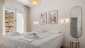 Una cama bien tendida con sábanas y toallas blancas, un espejo en la pared y dos cuadros enmarcados.
