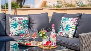 A glass table with wine glasses, a bottle, and decorative items on a balcony with a sofa and patterned cushions. - House Doris Hofmann Sa Ràpita with Pool (Sa Rapita)
