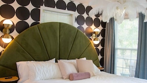 A bedroom with a green upholstered headboard, a round bed with white bedding, a round rug, and a wall with circular patterns.