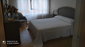 Un dormitori amb un llit, una nit, una làmpada, una cadira, una petita taula i un mirall.