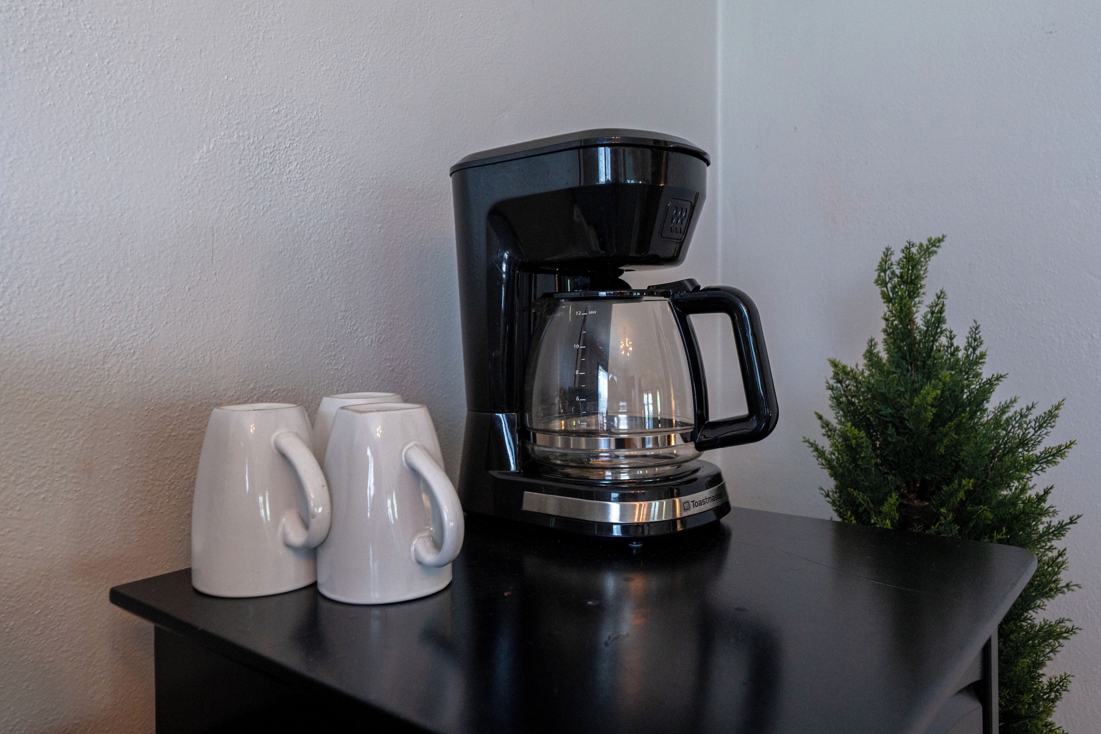 A black coffee maker with a glass carafe on a black countertop, accompanied by two white mugs.
