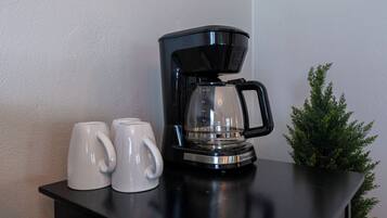 A black coffee maker with a glass carafe on a black countertop, accompanied by two white mugs.
