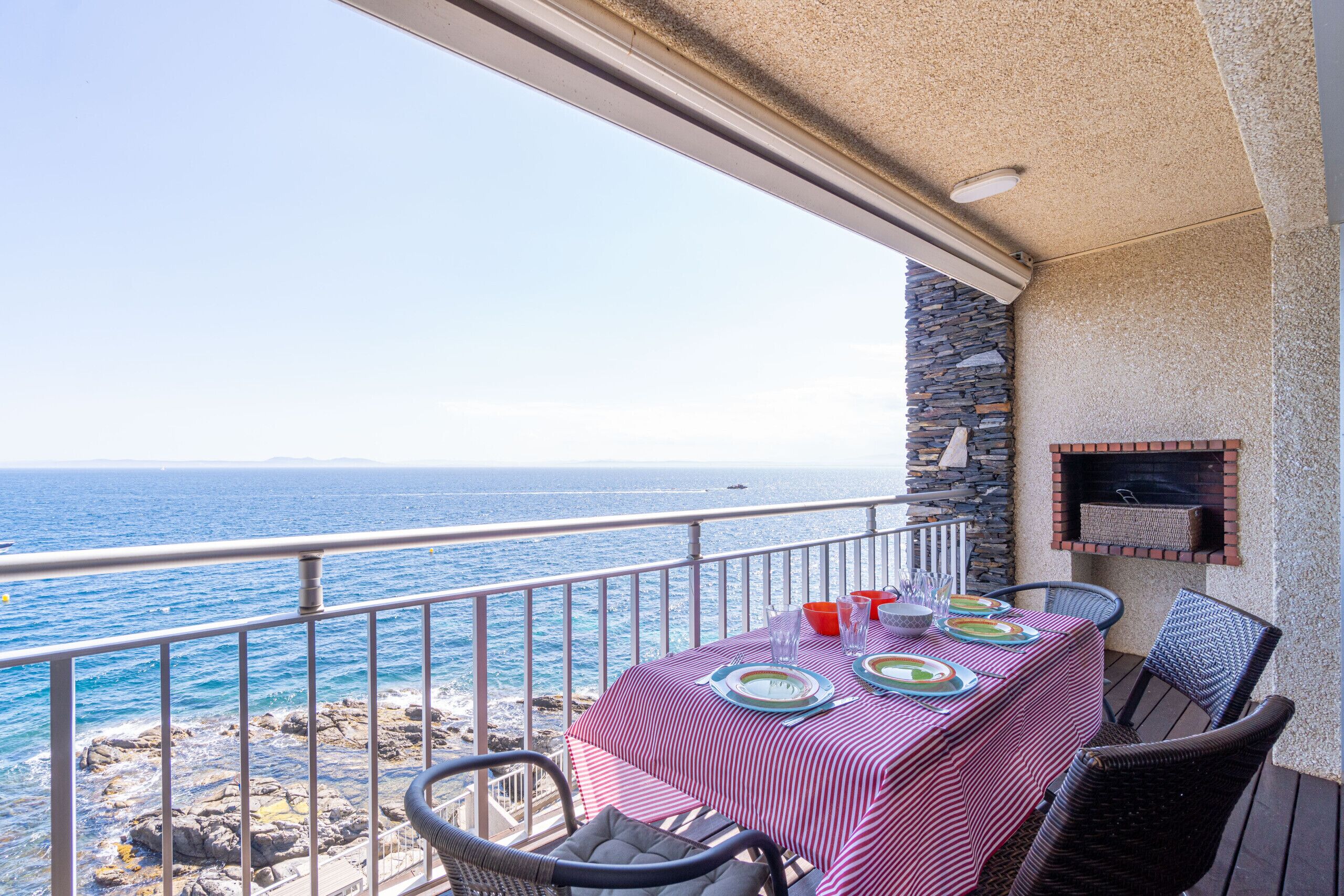A balcony with a table set for dining, overlooking the sea.