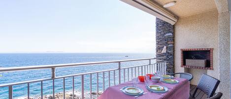 A balcony with a table set for dining, overlooking the sea.