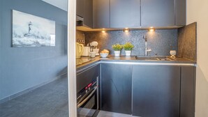 Eine moderne Küche mit dunklen Schränken, einer Arbeitsplatte aus Granit, einer Kaffeemaschine, einem Spülbecken und zwei Topfpflanzen.