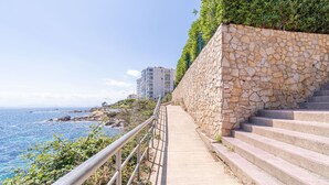 Eine Steintreppe führt hinab zu einer Küstenregion, mit freiem Blick auf das Meer und einem Gebäude im Hintergrund.