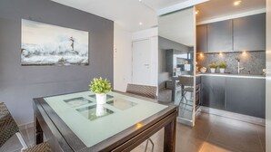 Eine moderne Küche mit Edelstahlgeräten, einem Glastisch mit Topfpflanze und einem Gemälde eines Leuchtturms an der Wand.