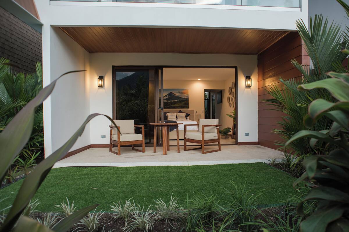 A modern house with a patio area featuring a table and chairs, surrounded by well-maintained greenery.