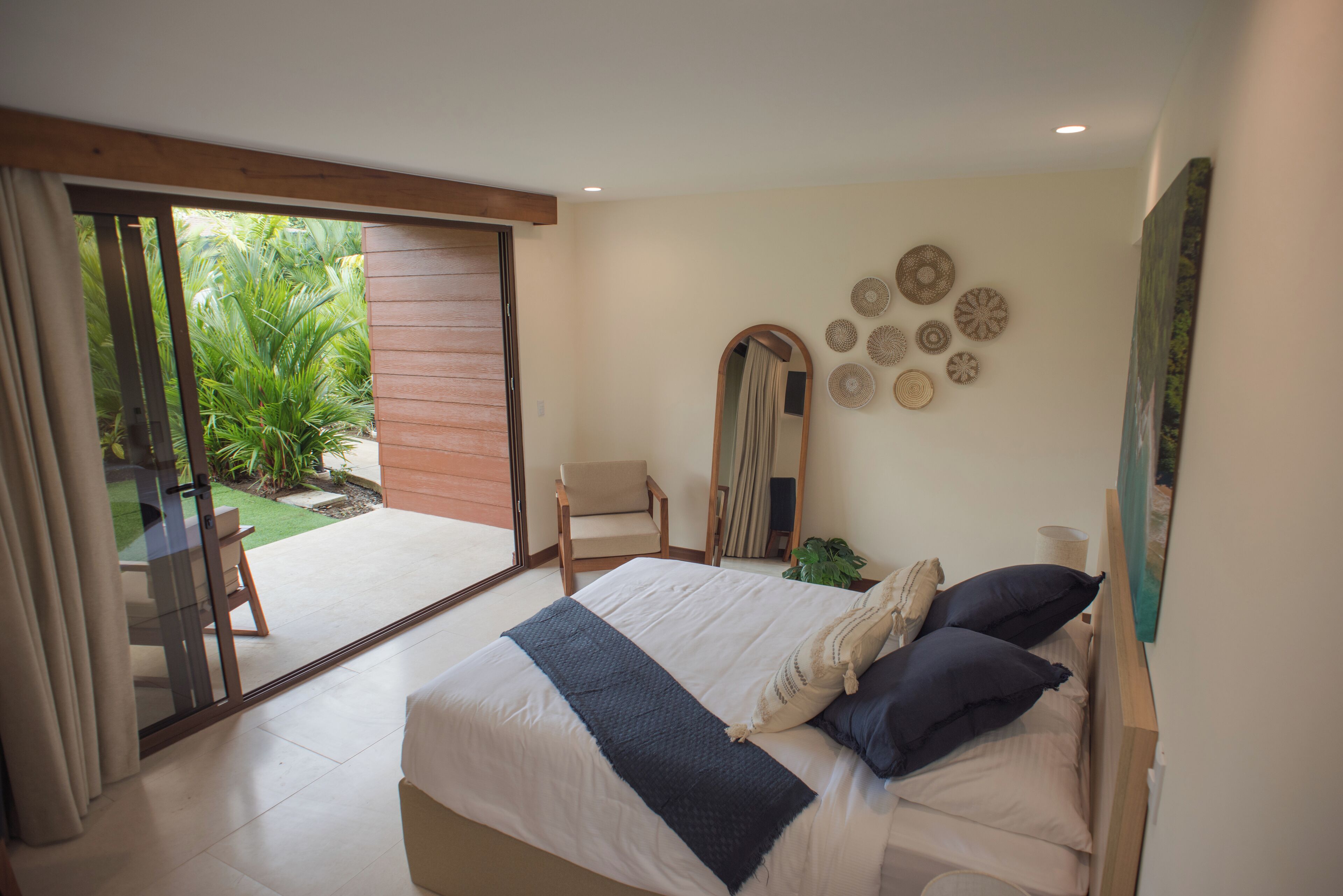 Un dormitorio con una cama grande, una puerta corrediza a un patio, una silla y un muro decorado con diseños circulares.