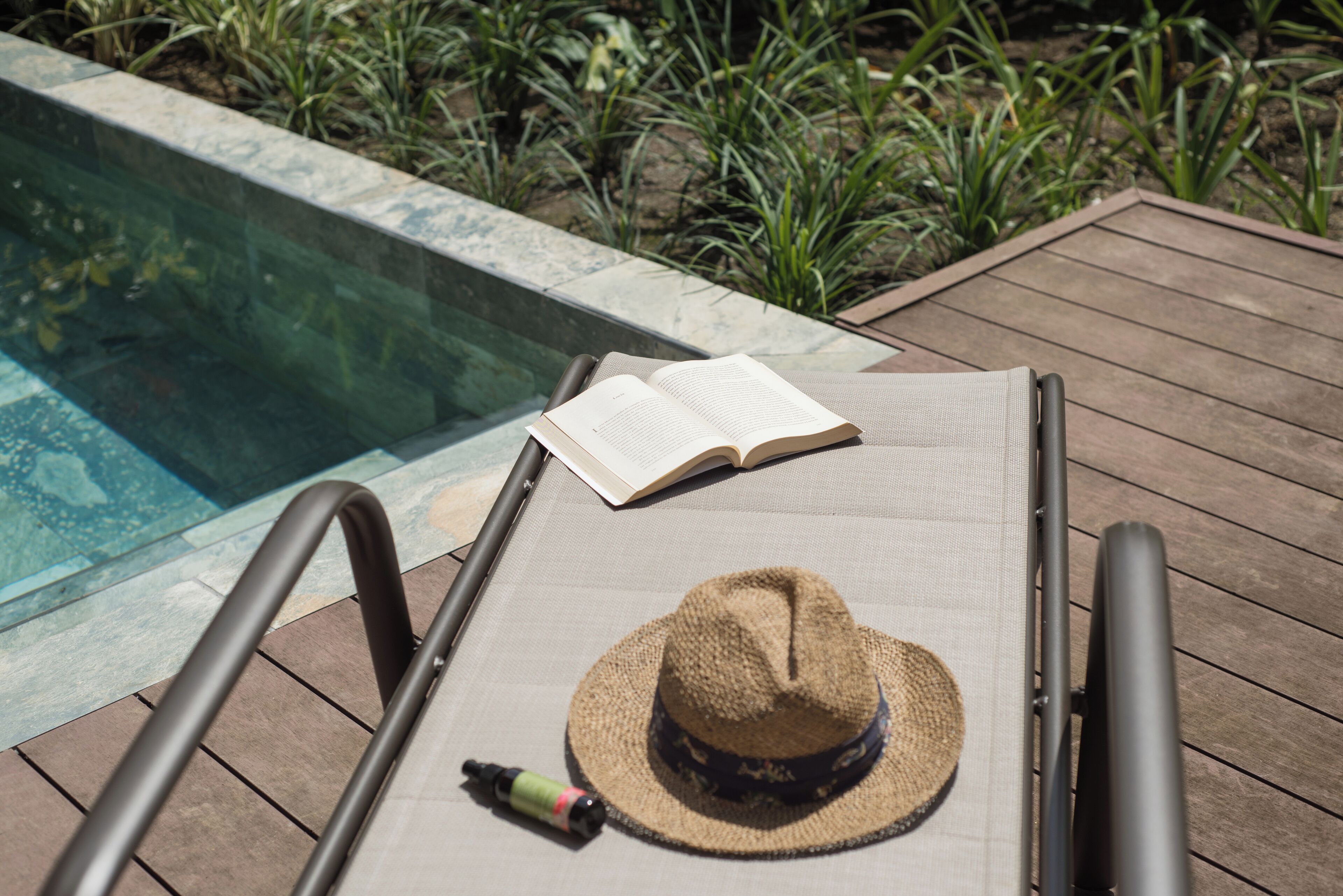 A lounge chair with a hat and an open book by a pool.