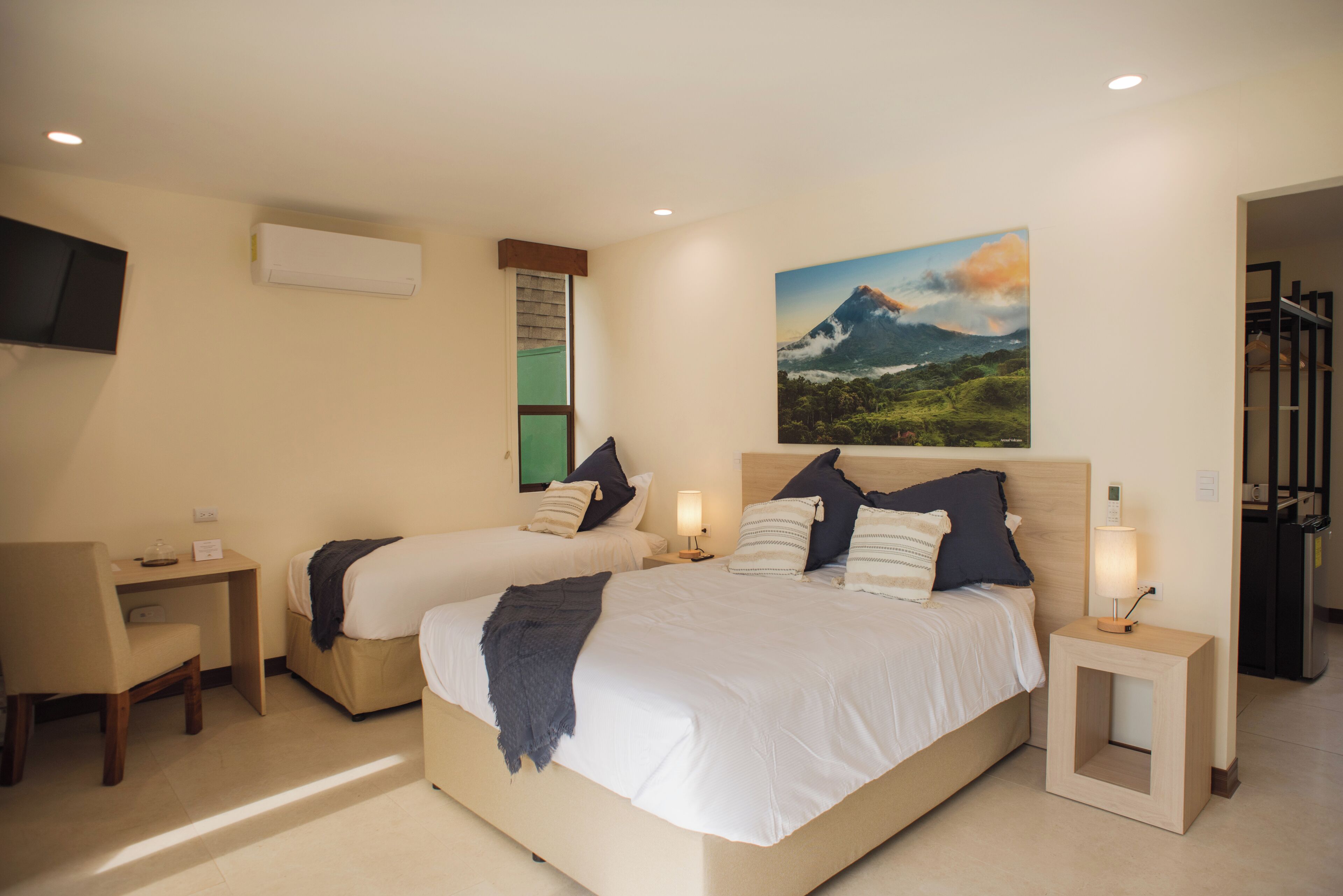 Habitación de hotel con dos camas, un escritorio, una silla, un televisor y un cuadro en la pared.