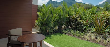 A patio with a wooden table and a chair, surrounded by lush greenery and a view of mountains.