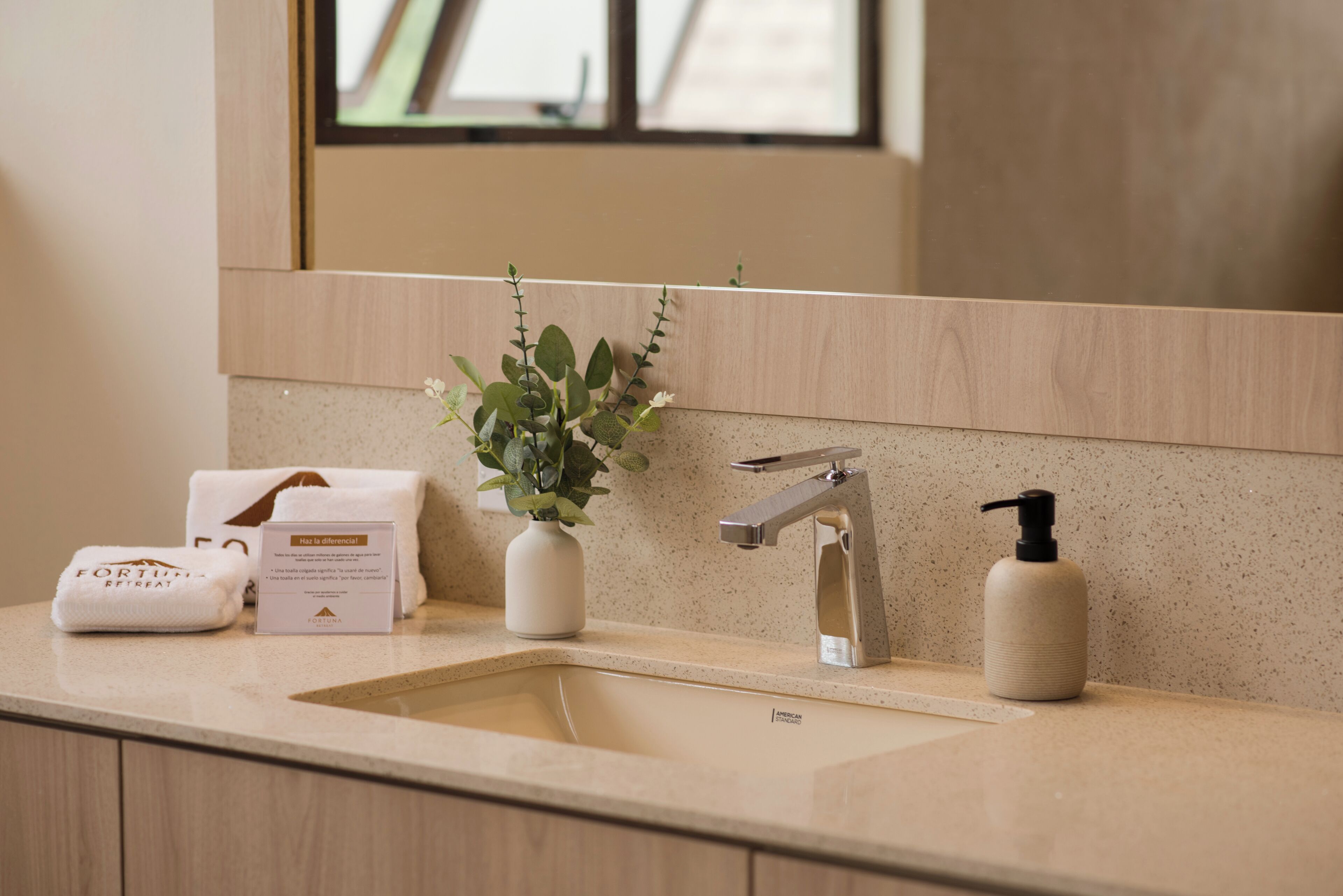 A bathroom with a sink, a mirror, a plant, a towel, and a bottle of soap.