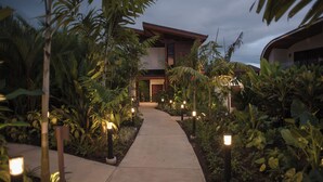 A pathway leading to a modern house surrounded by lush tropical plants and illuminated by ground lights. - Fortuna Retreat (La Fortuna)