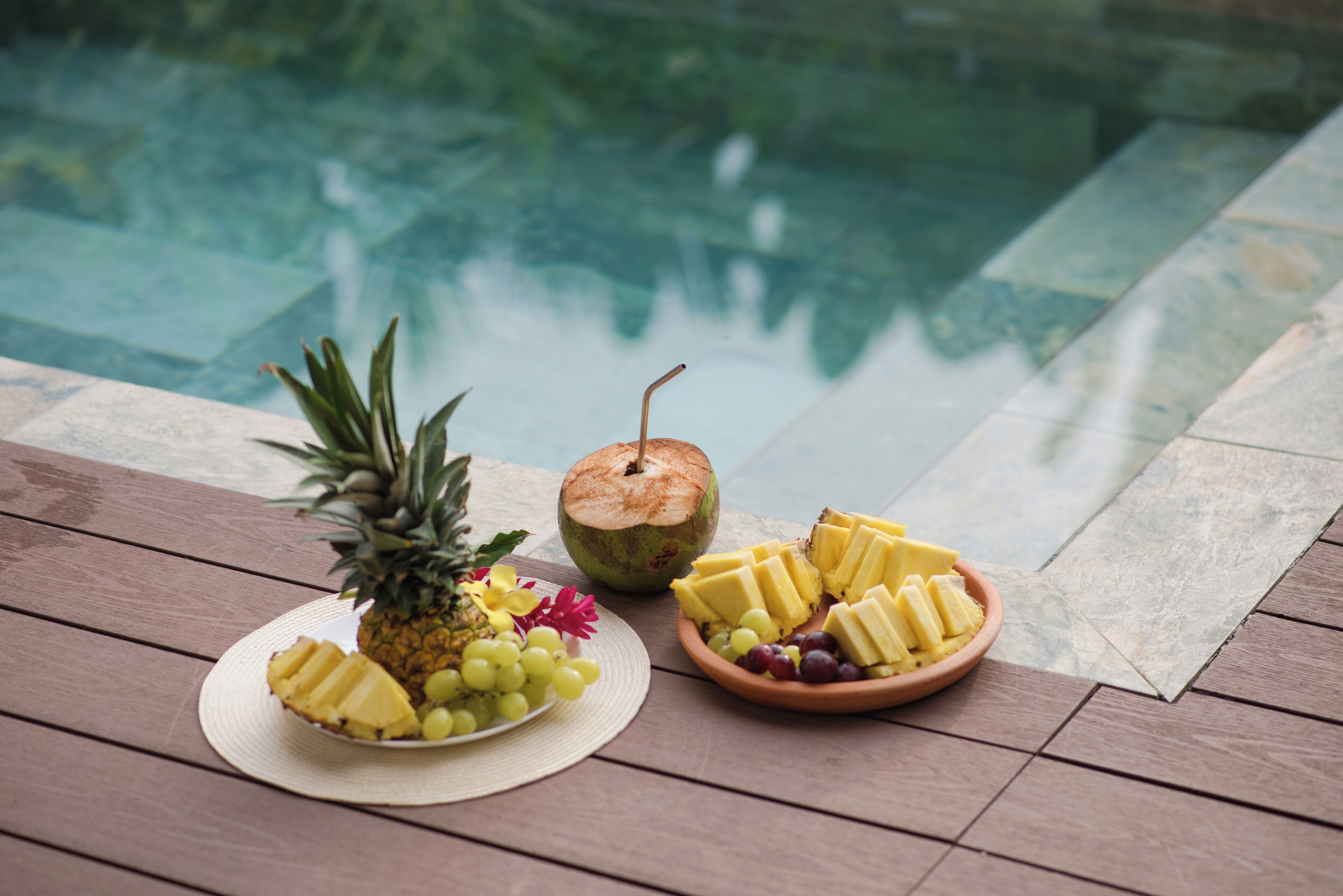 A wooden deck with a fruit platter, a pineapple, and a coconut.