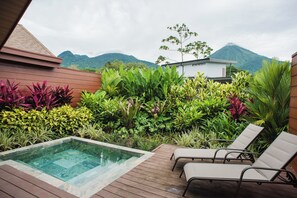 Un espace piscine doté de chaises longues, entouré d’une végétation luxuriante et offrant une vue sur les montagnes.