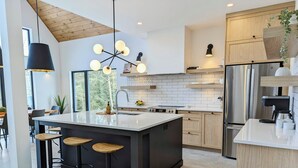 Une cuisine moderne dotée d’un îlot central, de tabourets de bar, d’un luminaire suspendu et d’un réfrigérateur en acier inoxydable.