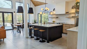 Une cuisine moderne dotée d’un grand îlot central, de tabourets de bar, de luminaires suspendus et offrant une vue sur l’extérieur.