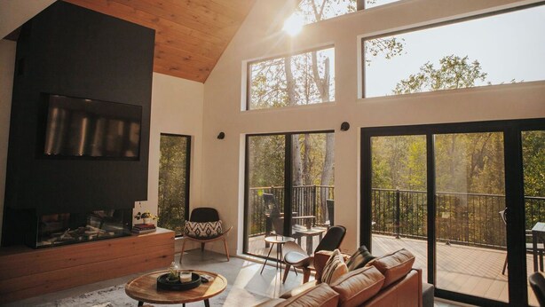 Un salon moderne doté d’une cheminée, de grandes fenêtres et d’un balcon aménagé avec du mobilier d’extérieur.