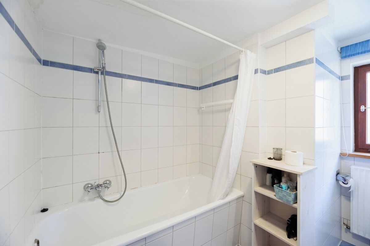 A bathroom with a bathtub, shower, and a toilet. There is a shelf with toiletries.